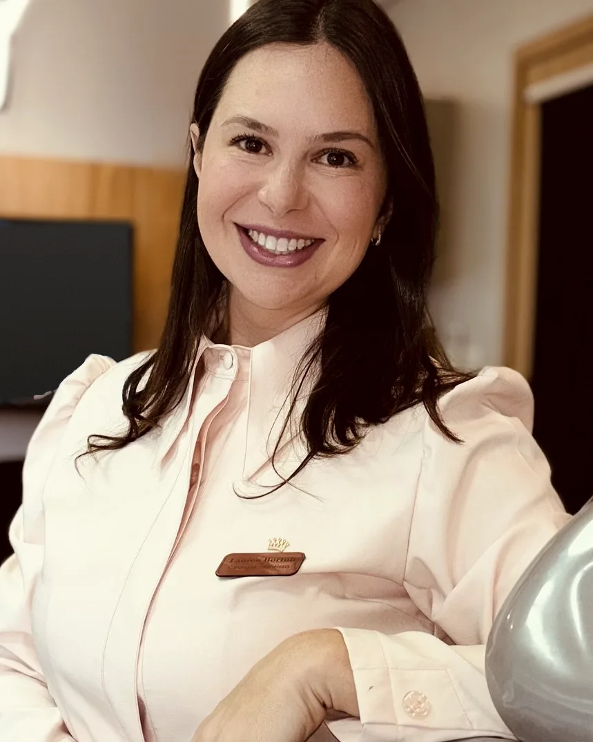 Dra. Lauren Bortoli no consultório, sorrindo, apoiada na cadeira odontológica